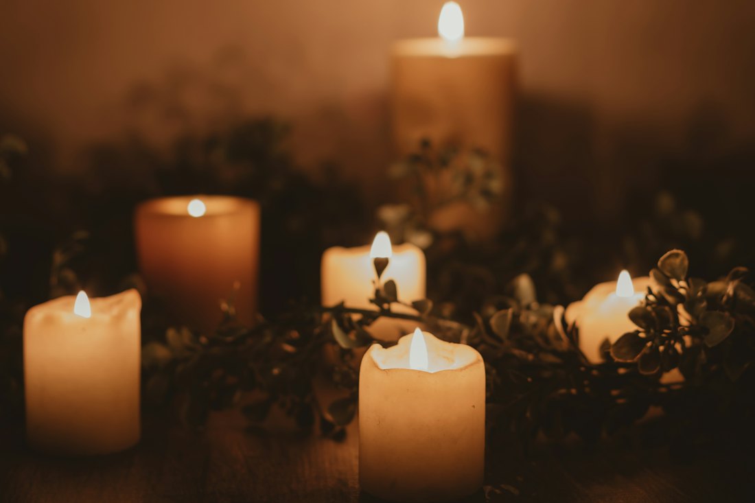 A cluster of glowing pillar candles of different heights surrounded by trailing greenery in a dim room