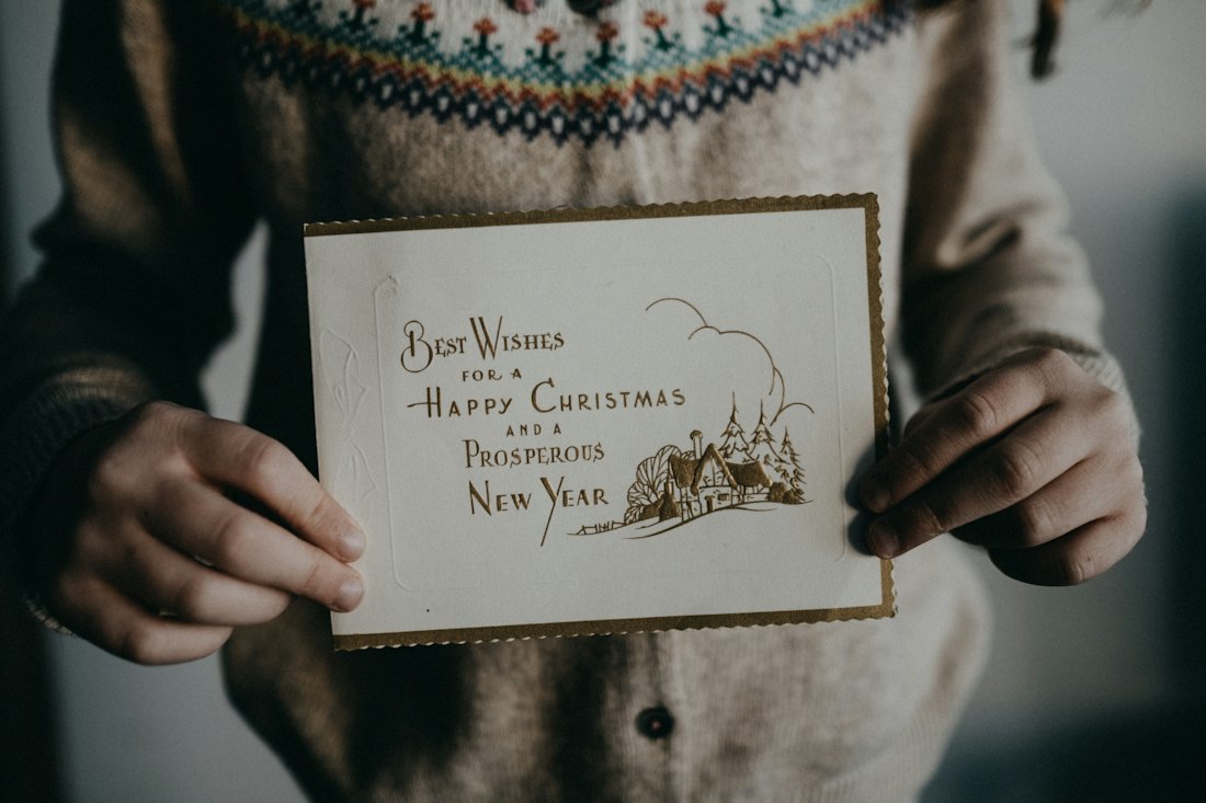 Hands holding a cream vintage-style Christmas card with gold lettering wishing a happy Christmas and a prosperous New Year