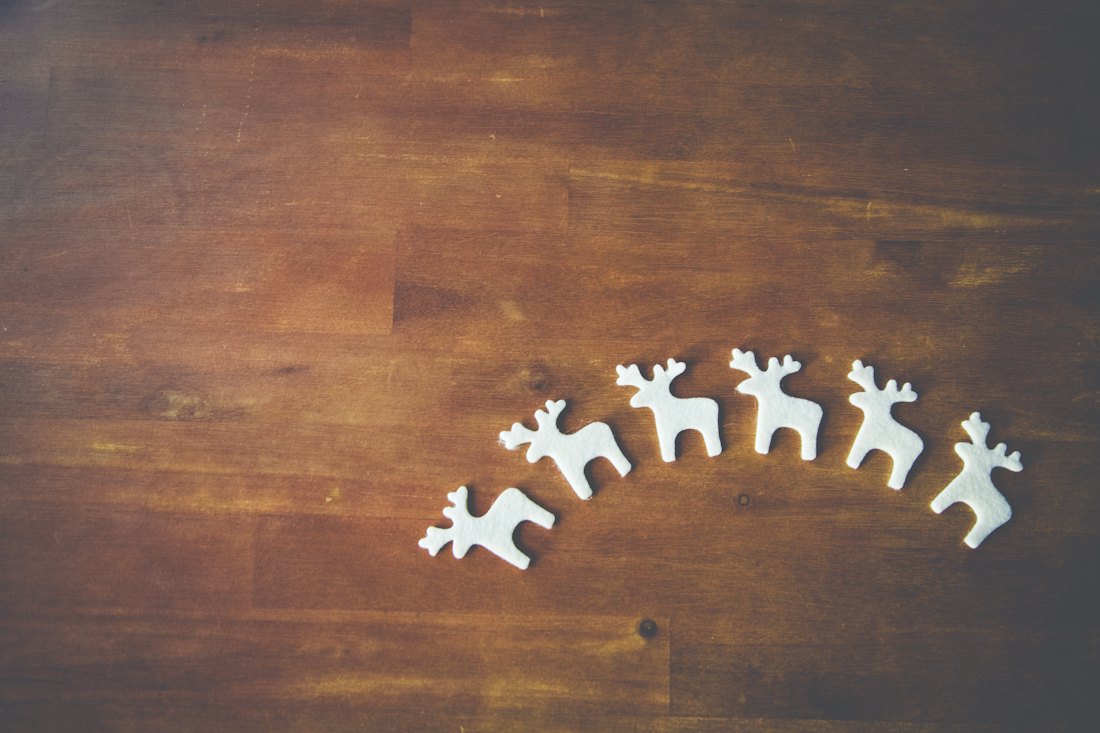 A row of small white wooden reindeer decorations arranged in an arc on a dark wooden surface