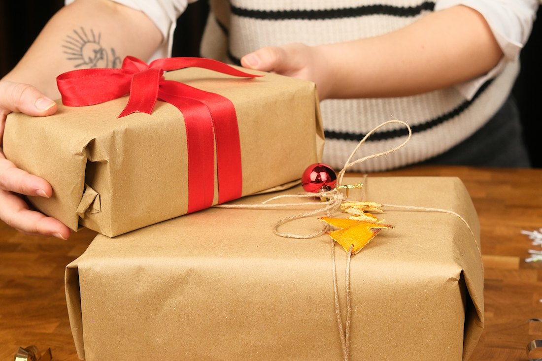 Two gifts wrapped in plain kraft paper, one tied with red ribbon and one with natural twine and a dried orange decoration