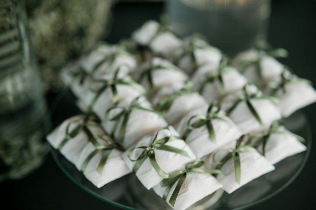 Small white wrapped favours tied with thin green ribbon arranged on a glass platter