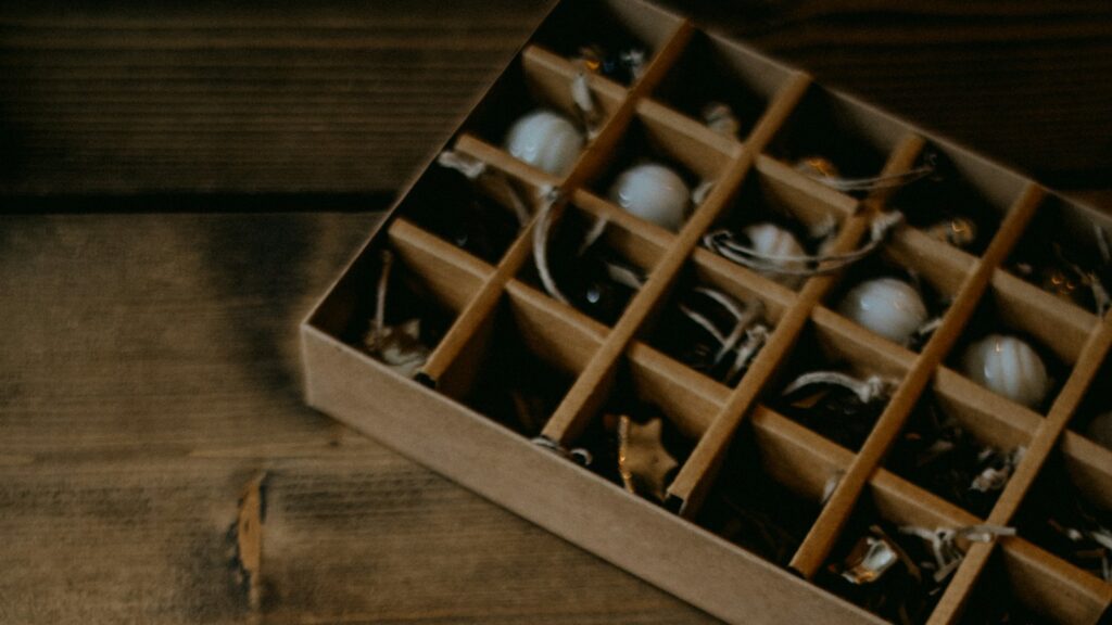 A kraft-paper box with compartments holding white and silver ornaments on a dark wooden table