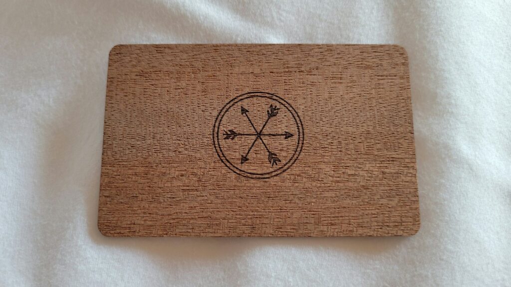 A wooden card engraved with a simple circular compass design resting on soft white fabric