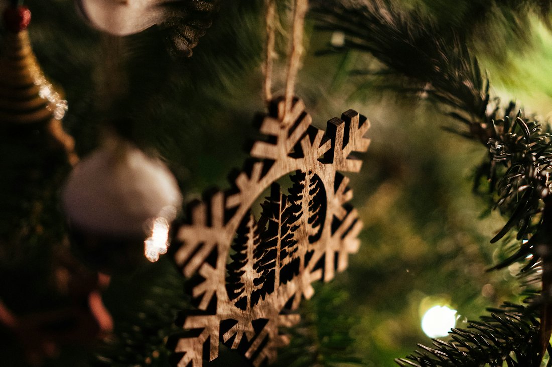 A laser-cut wooden snowflake decoration hanging on twine among the branches of a softly lit Christmas tree