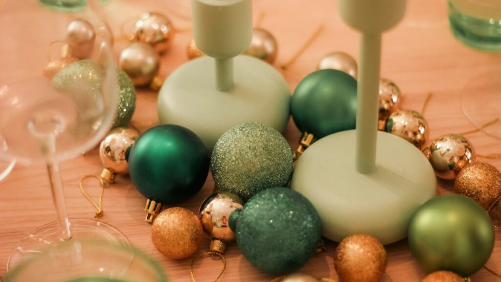 Green and gold baubles scattered around sage green candle holders on a softly lit table