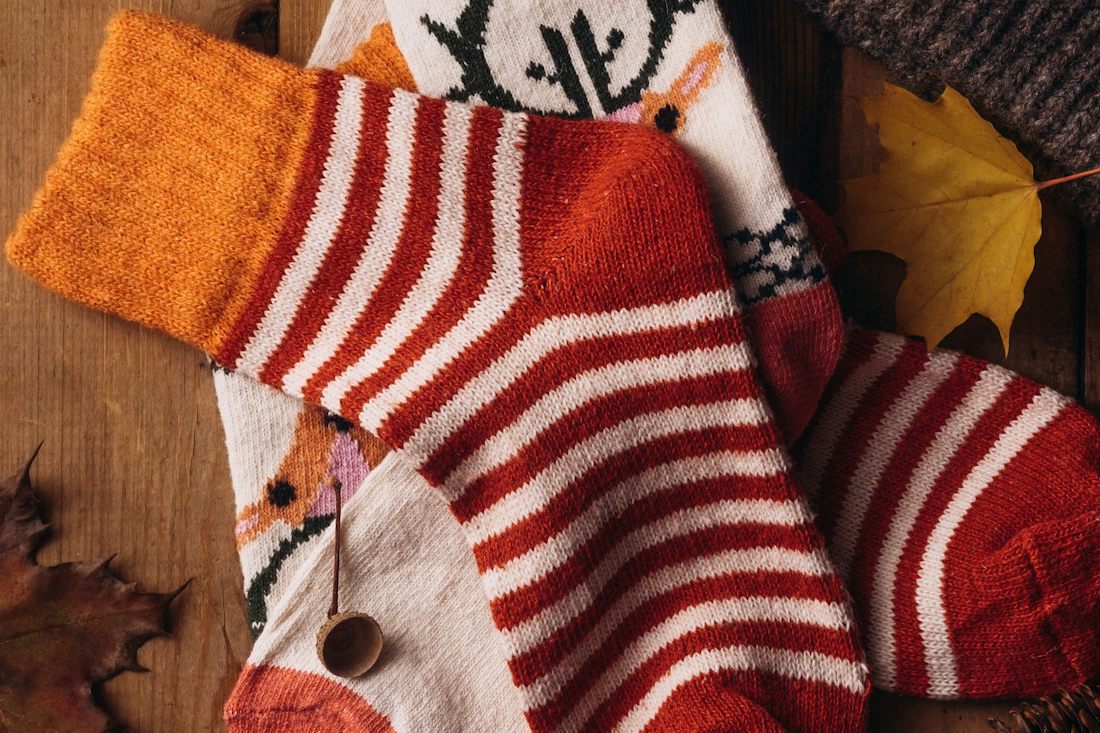 Striped and patterned knitted socks laid on a wooden surface with pine cones and fallen leaves